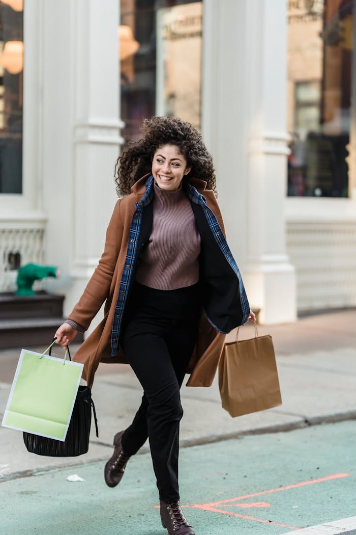 Cheerful ethnic woman with shopper bags running on road